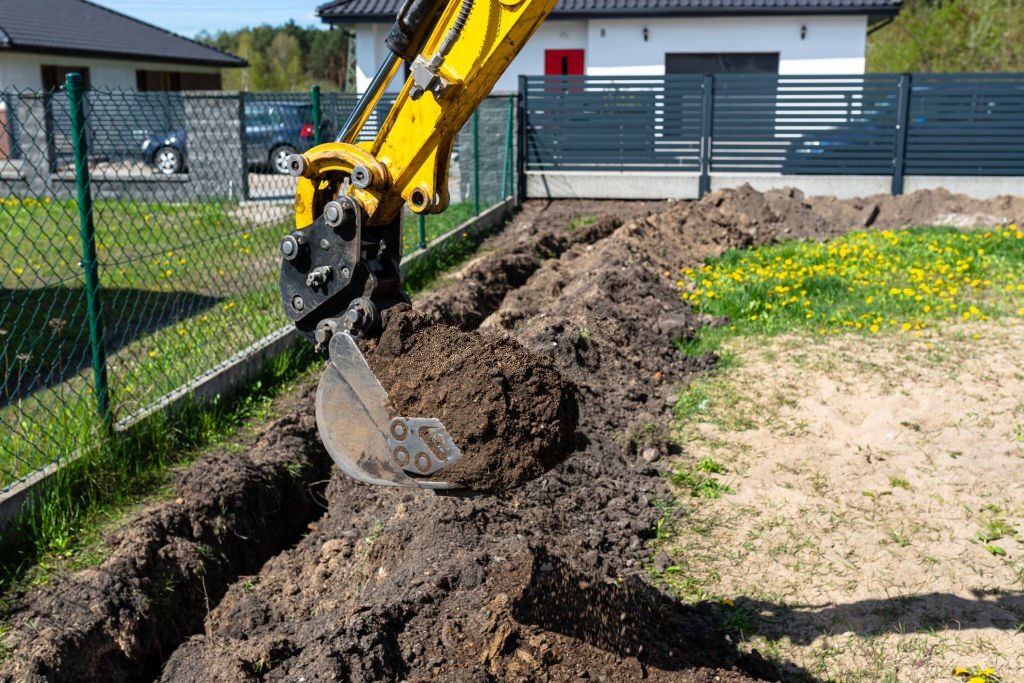 Mini digger digging a hole in the garden along the fence to the drainage pipes. Minibagr Ostrava