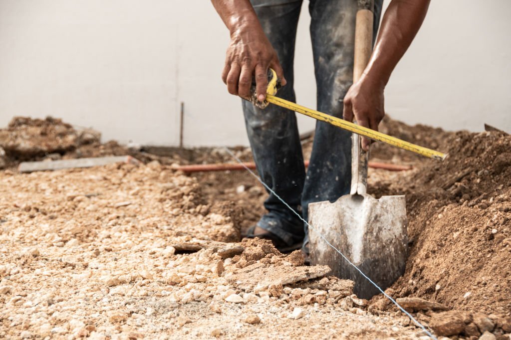 Man measuring and digging a hole in the ground with shovel Zemní práce